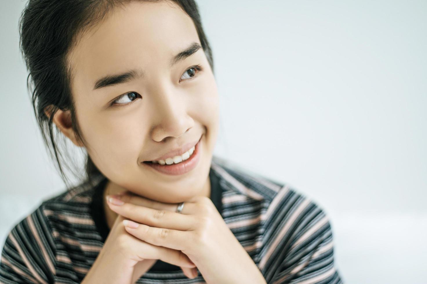 una mujer joven se sienta con las manos descansando debajo de la barbilla mientras sonríe foto