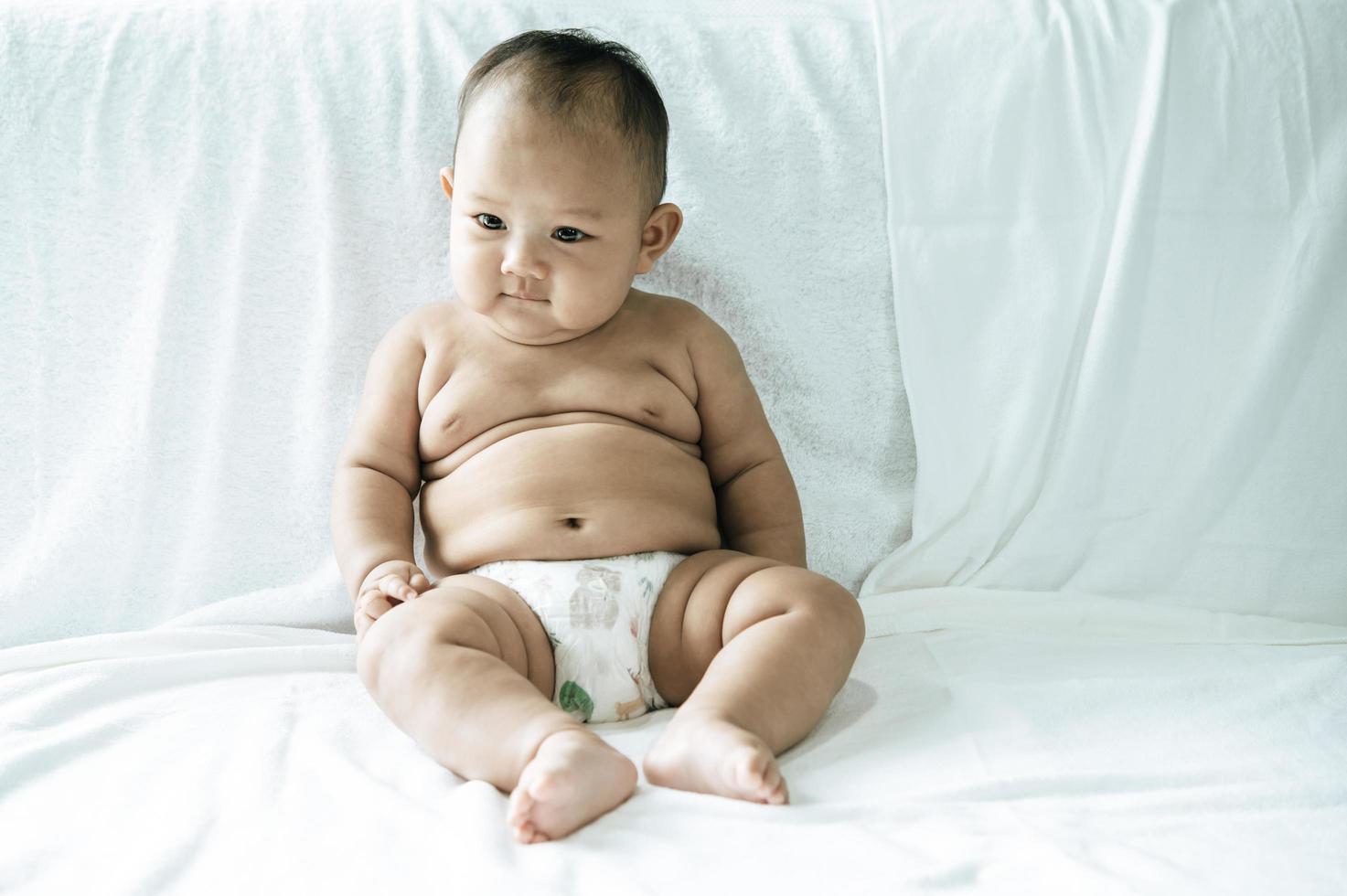 A baby learning to sit on a white bed photo