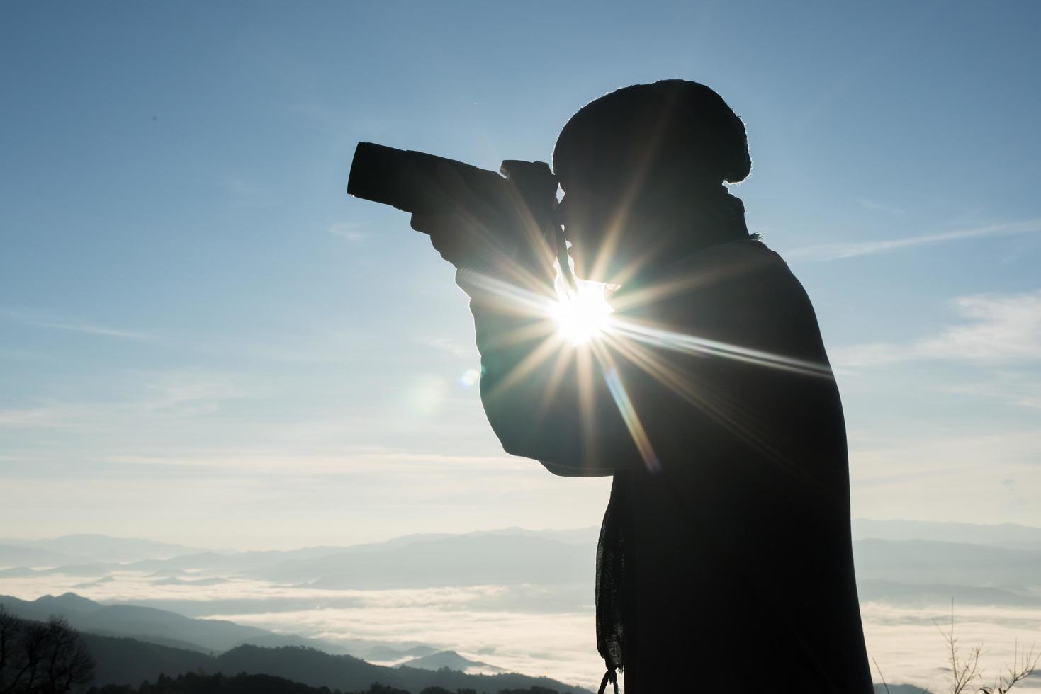 Silhouette of young photographer holding a camera with mountain landscape photo