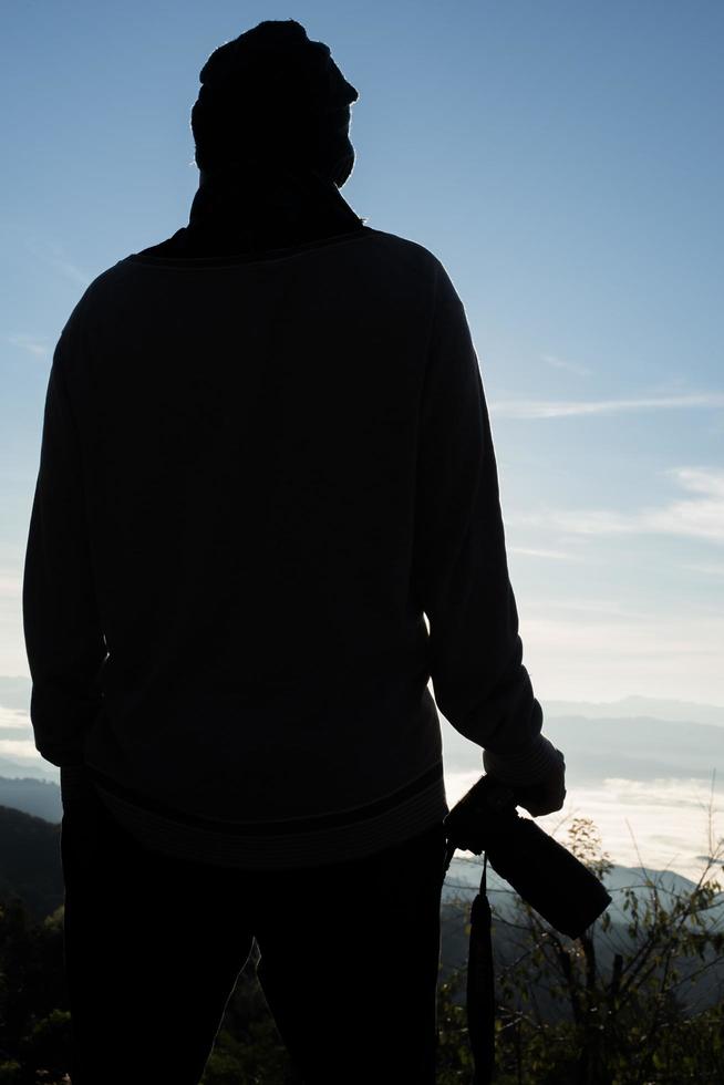 Silhouette of young photographer holding a camera with mountain landscape photo