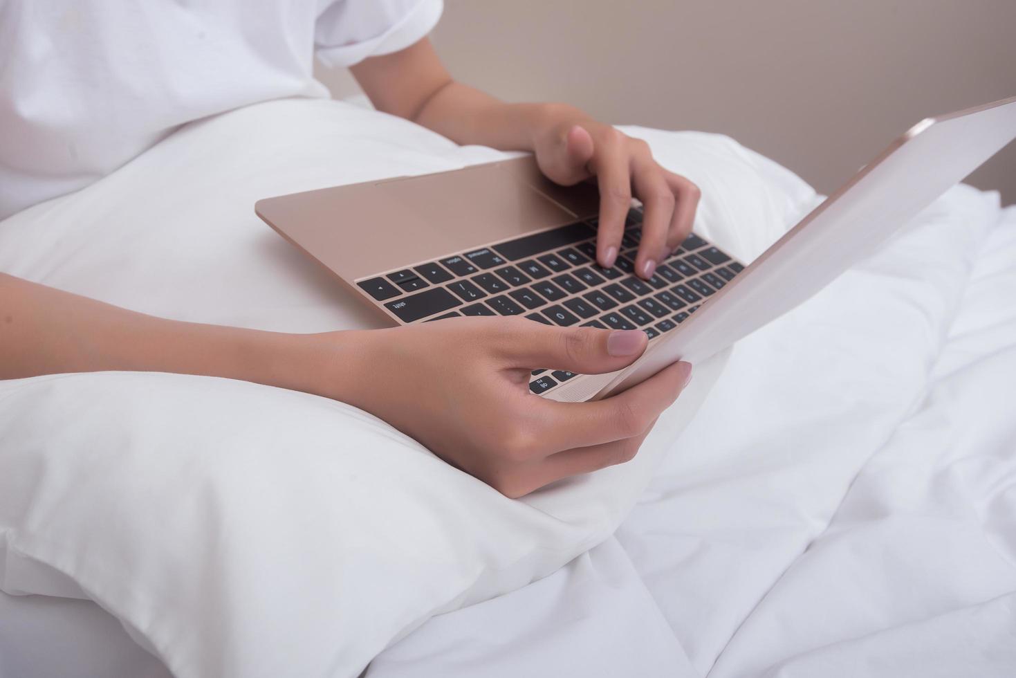 Mujer usando laptop mientras está sentado en la cama foto