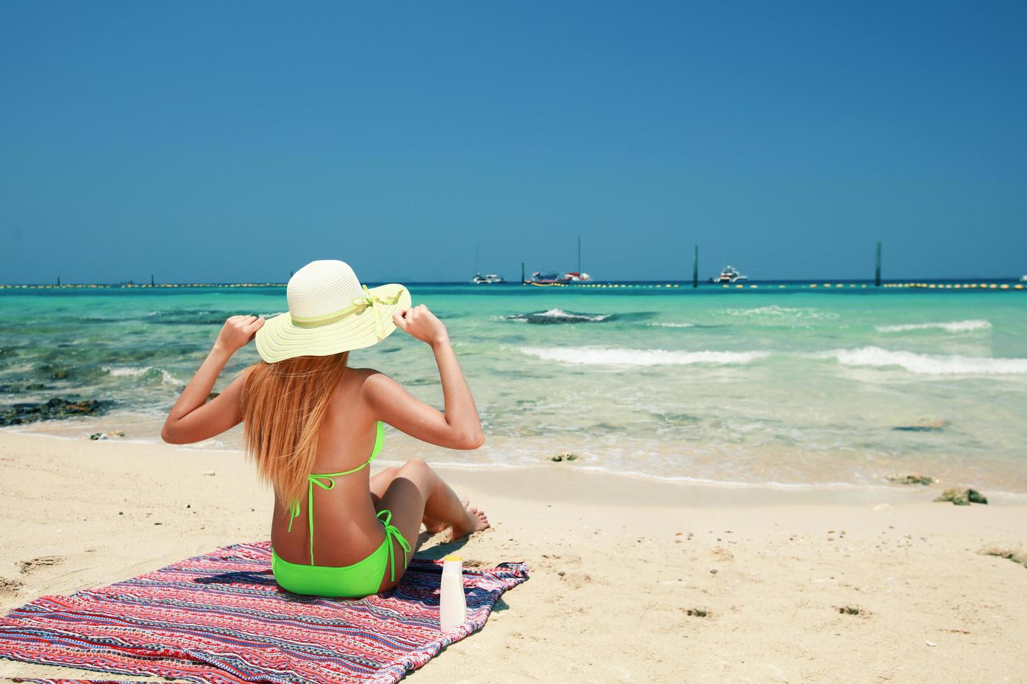 Vista posterior de una joven asiática vistiendo bikini y sombrero para tomar el sol en la playa. foto