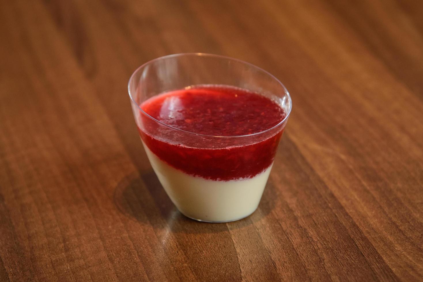 Delicioso postre italiano panna cotta con coulis de frambuesa en pequeños vasos transparentes foto