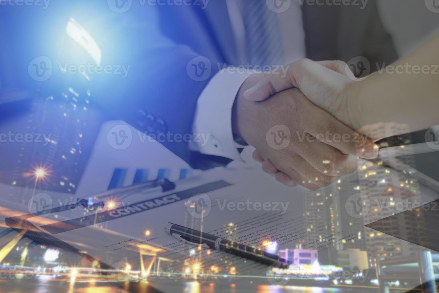Two businessmen shaking hands with night time city overlay photo