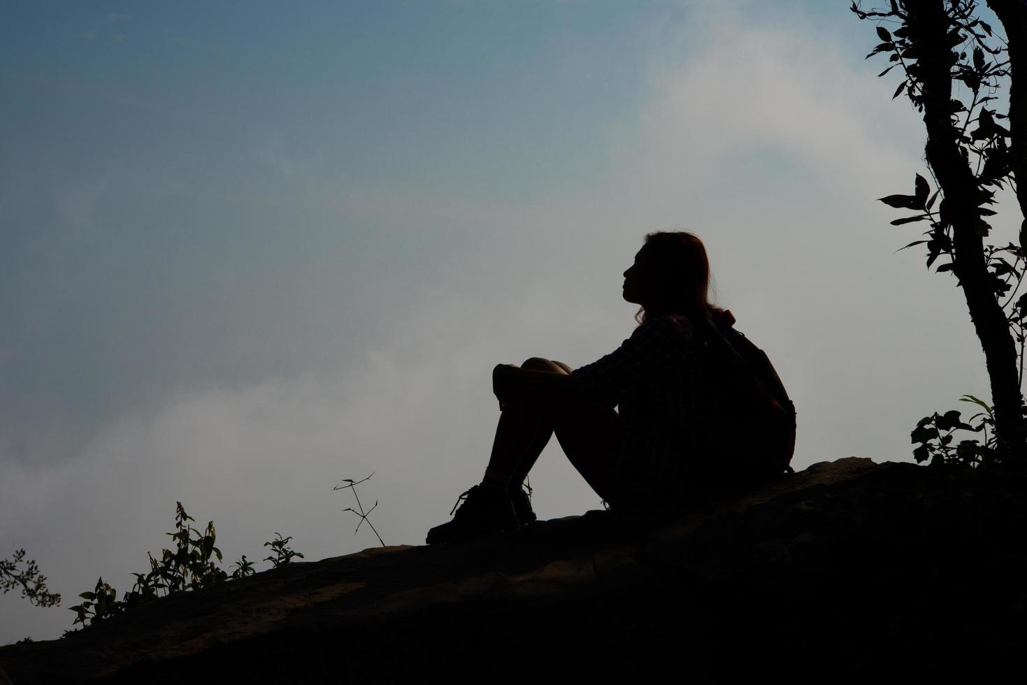 Silhouette of a hiker sitting on mountain top with blue sky background photo