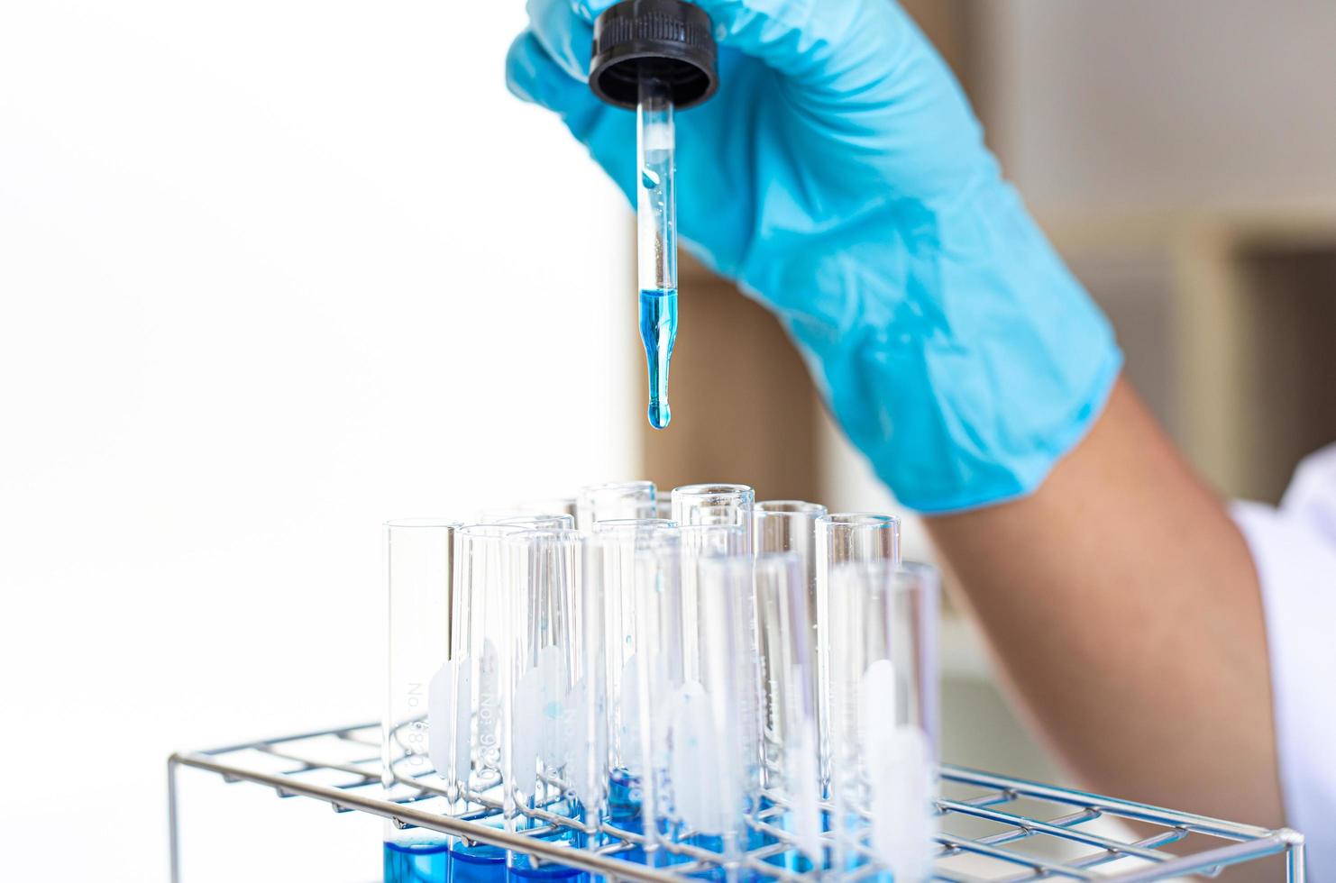 Scientist dropping blue liquid into test tubes photo