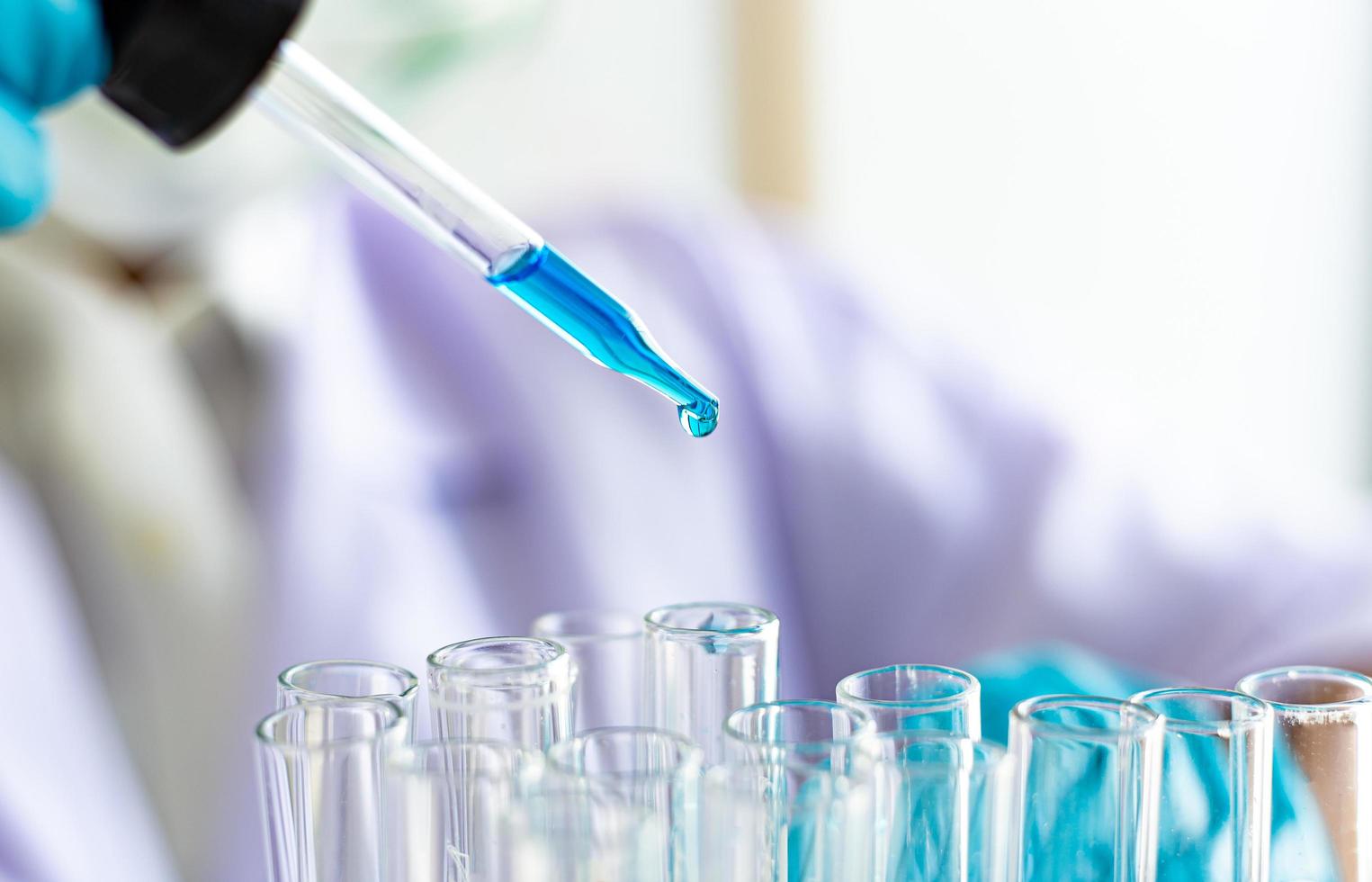 Scientist dropping blue liquid into test tubes photo