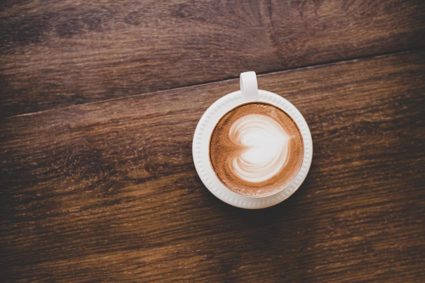 Top view of vintage latte art coffee with heart shape on wooden table photo