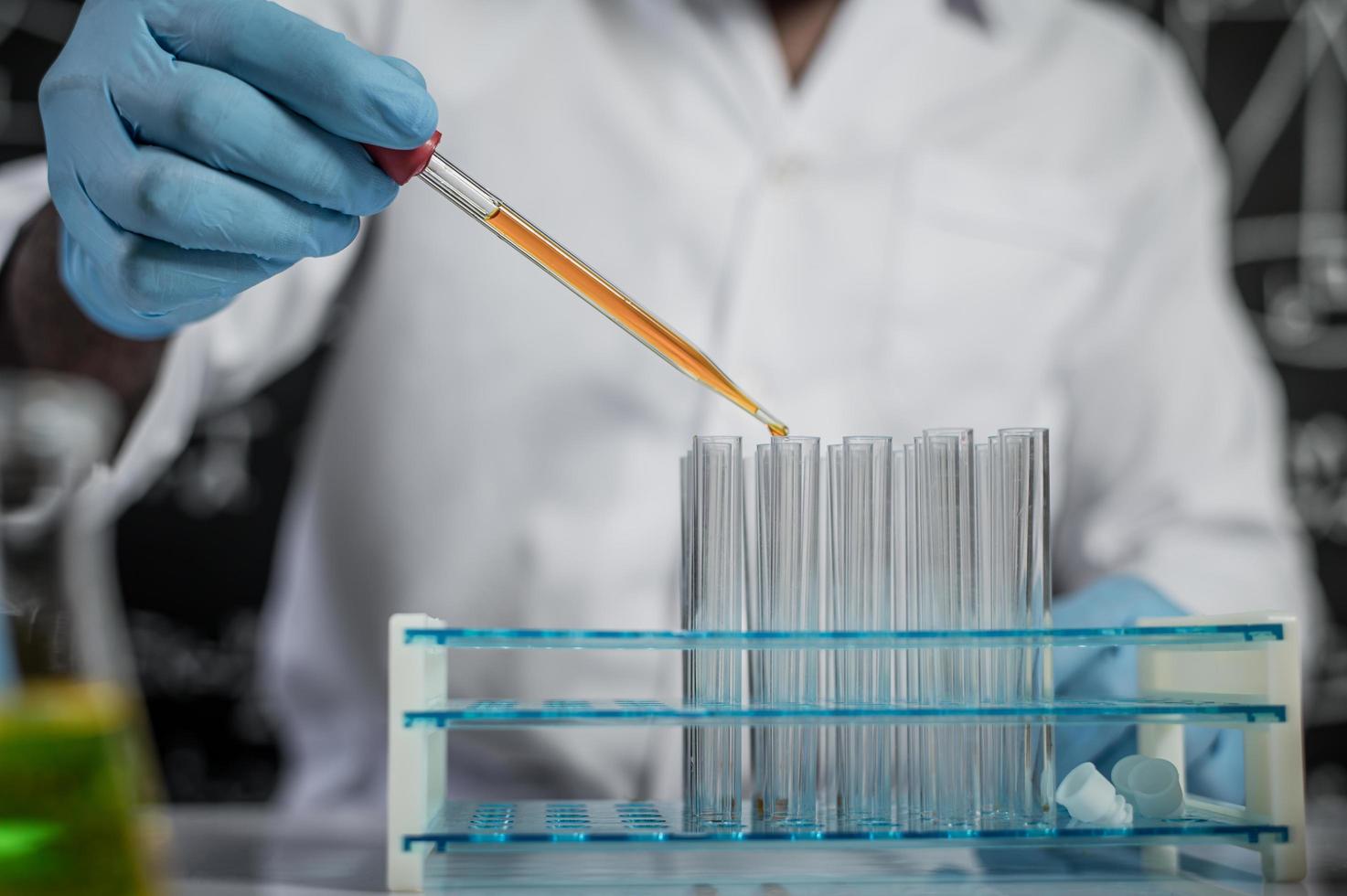 científico cae productos químicos de color naranja en vidrio en el laboratorio foto