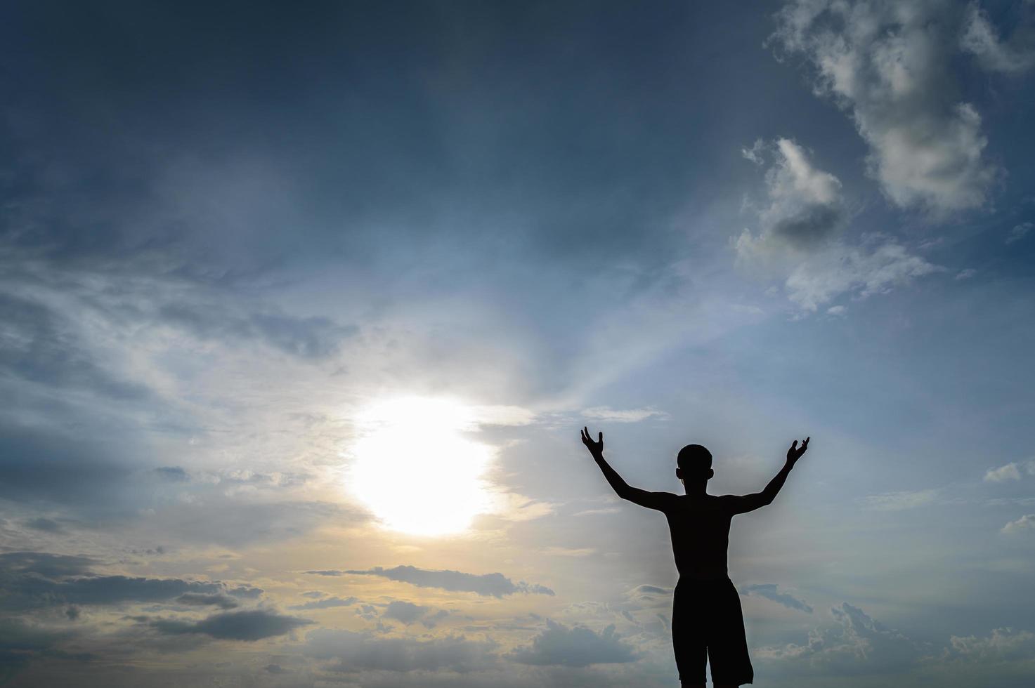 silueta de un niño levantando las manos en el cielo foto