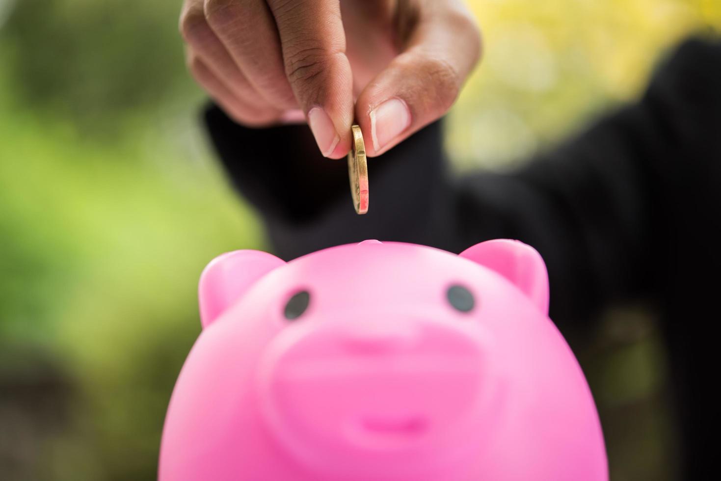 Person putting coins into a piggy bank on the table photo