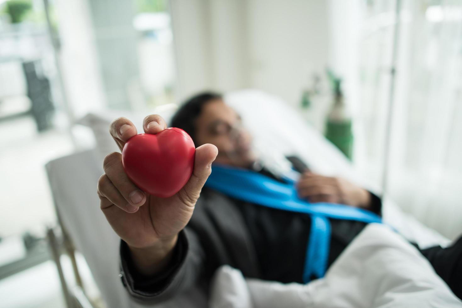 Hombre sujetando un corazón rojo en la mano en una cama de hospital foto
