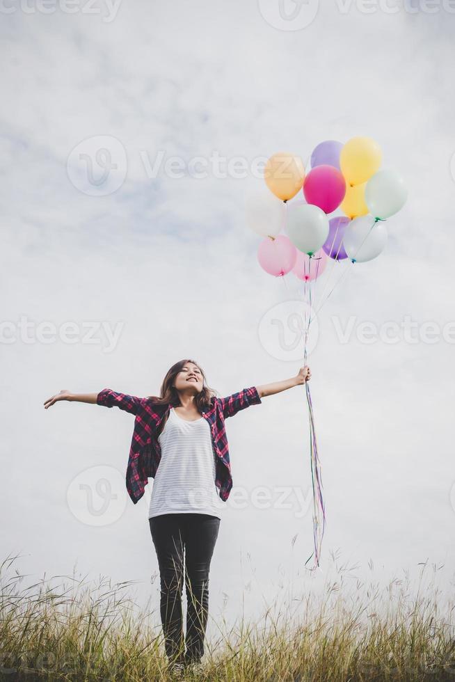 Beautiful young hipster woman holding colorful balloons outdoors photo