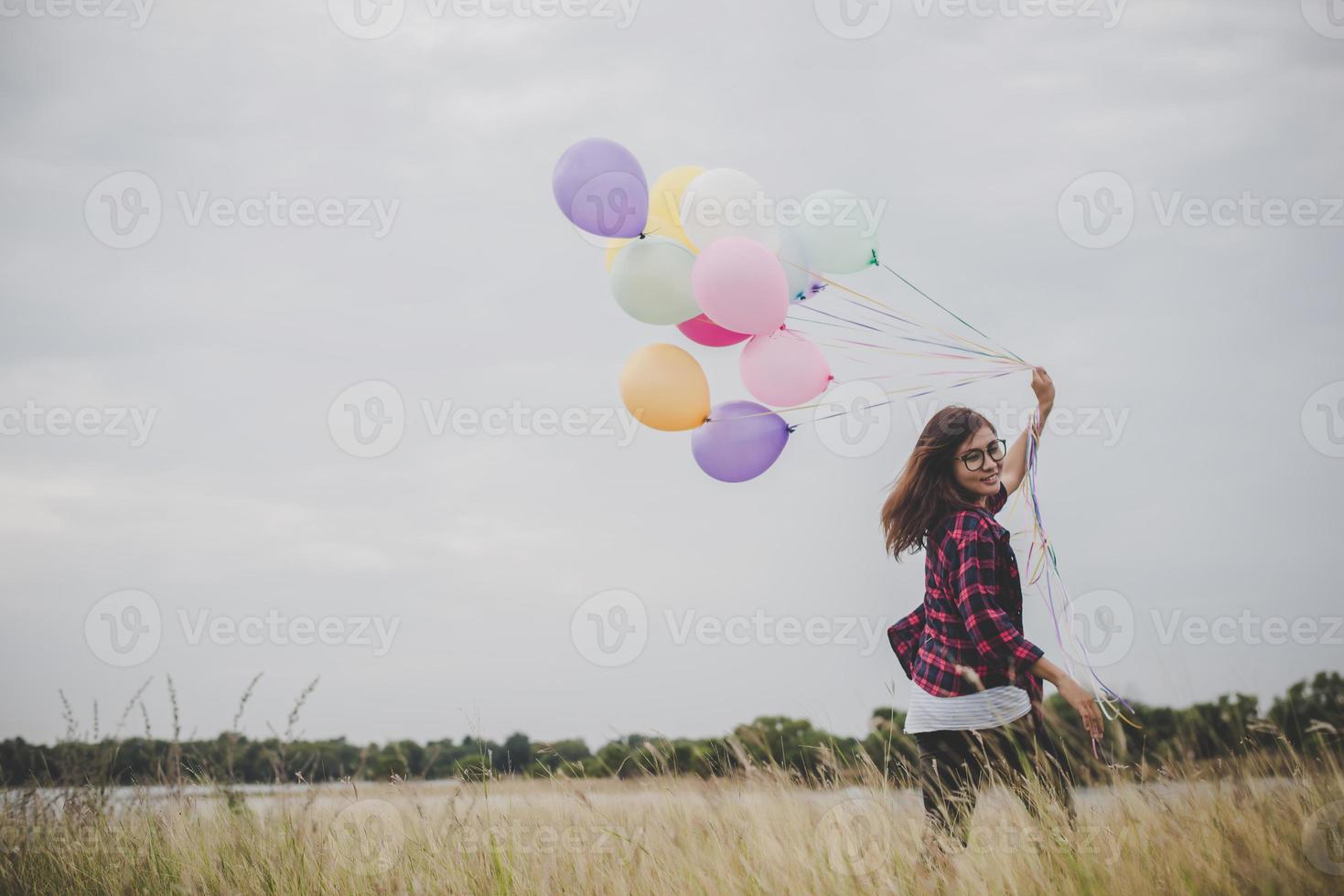 Beautiful young hipster woman holding colorful balloons outdoors photo