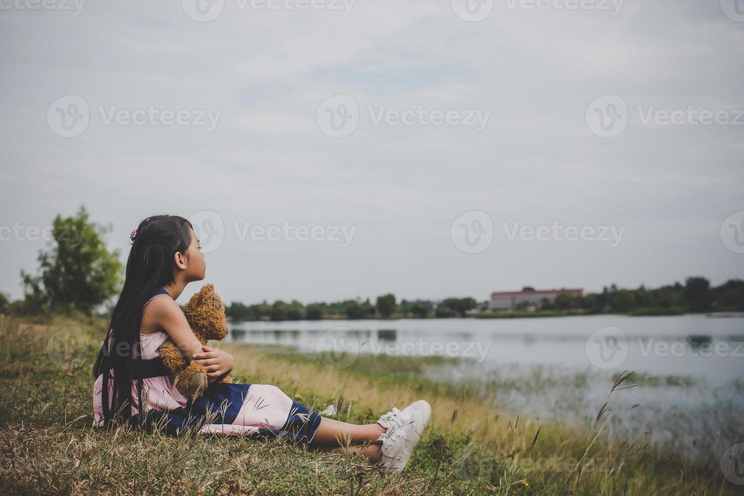 Little girl sitting with her bear upset in a meadow field photo