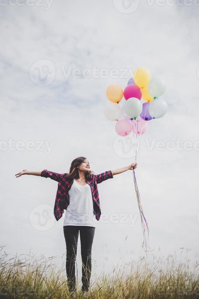 Beautiful young hipster woman holding colorful balloons outdoors photo