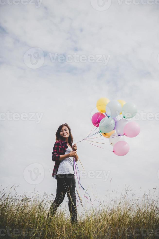 Beautiful young hipster woman holding colorful balloons outdoors photo