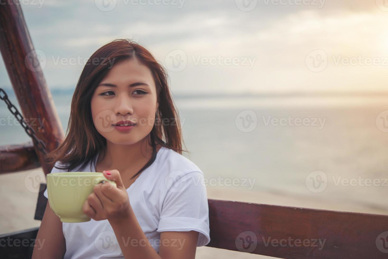 Bella mujer tomando café mientras está sentado en un columpio en la playa foto