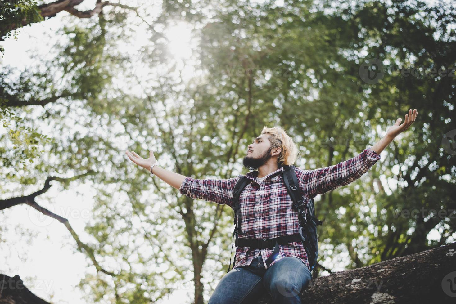 Young hiker hipster man sitting on a tree branch with arms stretched out photo