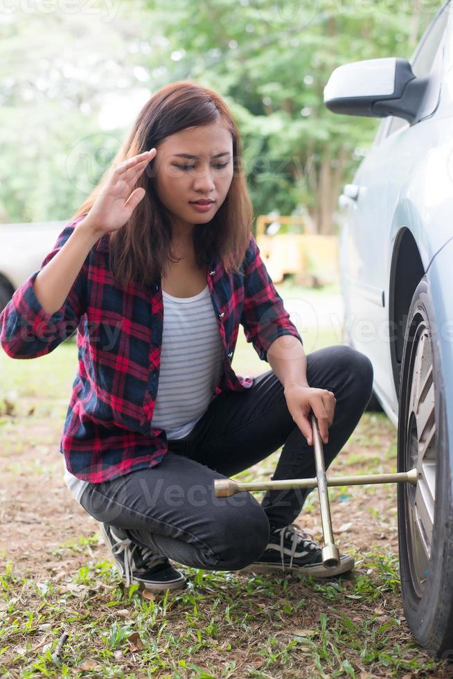 Mujer joven inconformista comprobando un pinchazo en su coche foto