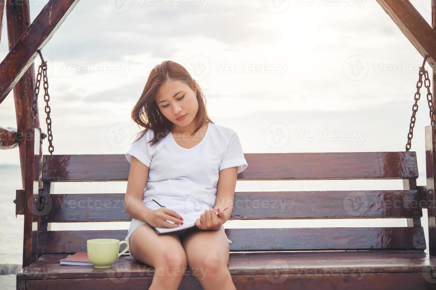 Hermosa joven escribiendo en el bloc de notas mientras está sentado en un banco foto