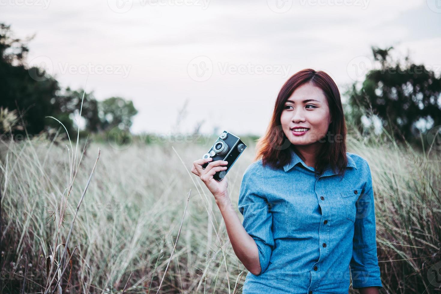 Happy young hipster woman with vintage camera in field photo