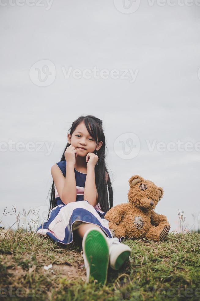 Linda chica asiática con osito de peluche sentado en un campo foto