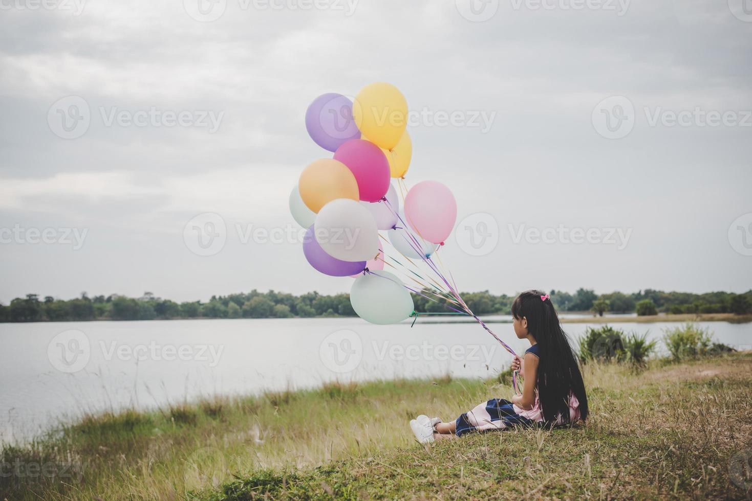 Little girl playing with balloons on meadow field photo