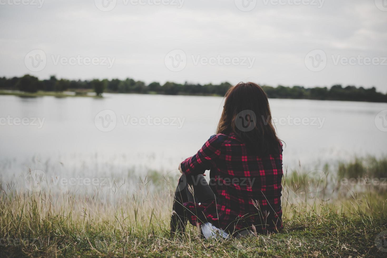 joven inconformista mujer sentada sobre la hierba cerca del lago relajante foto