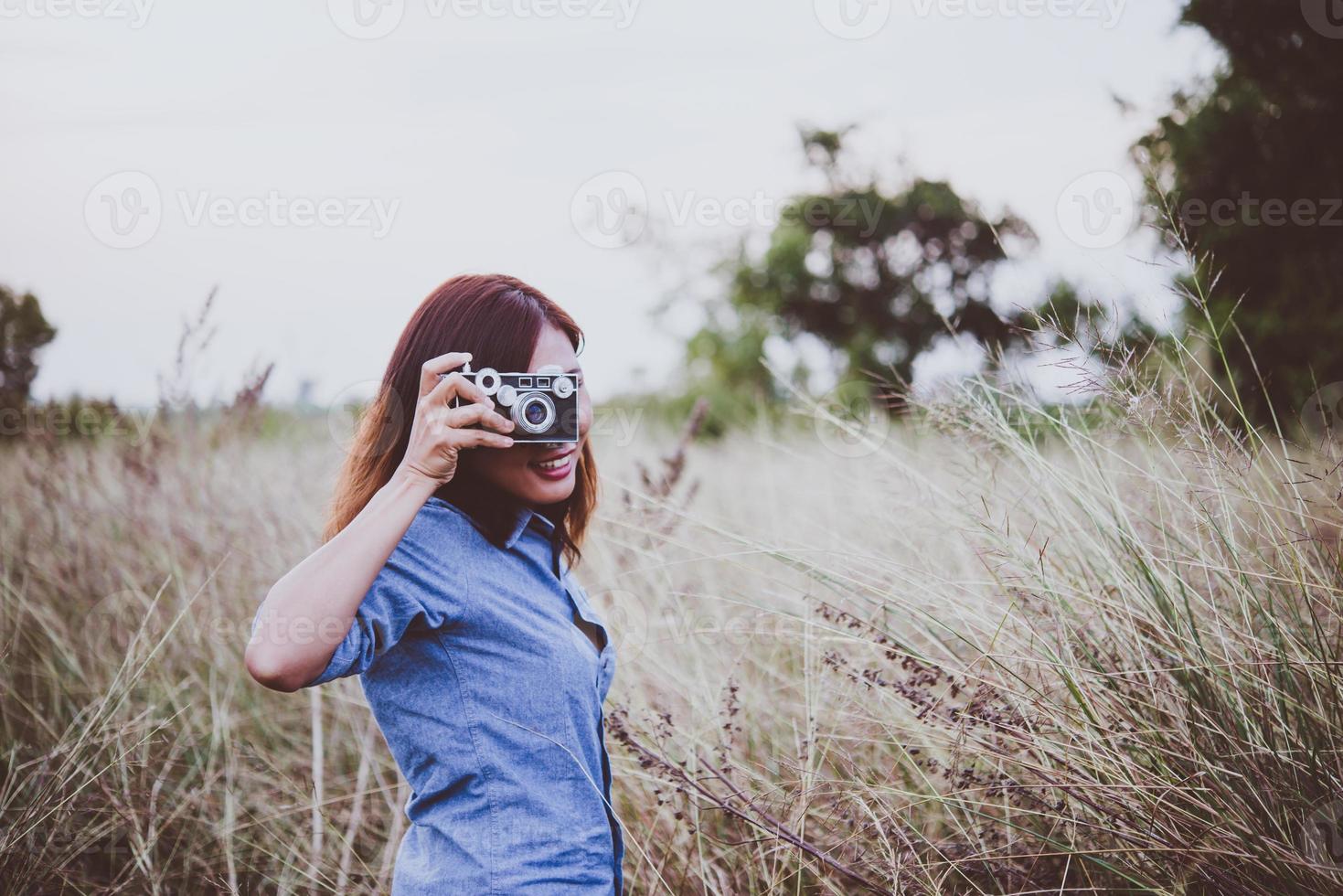 Happy young hipster woman with vintage camera in field photo