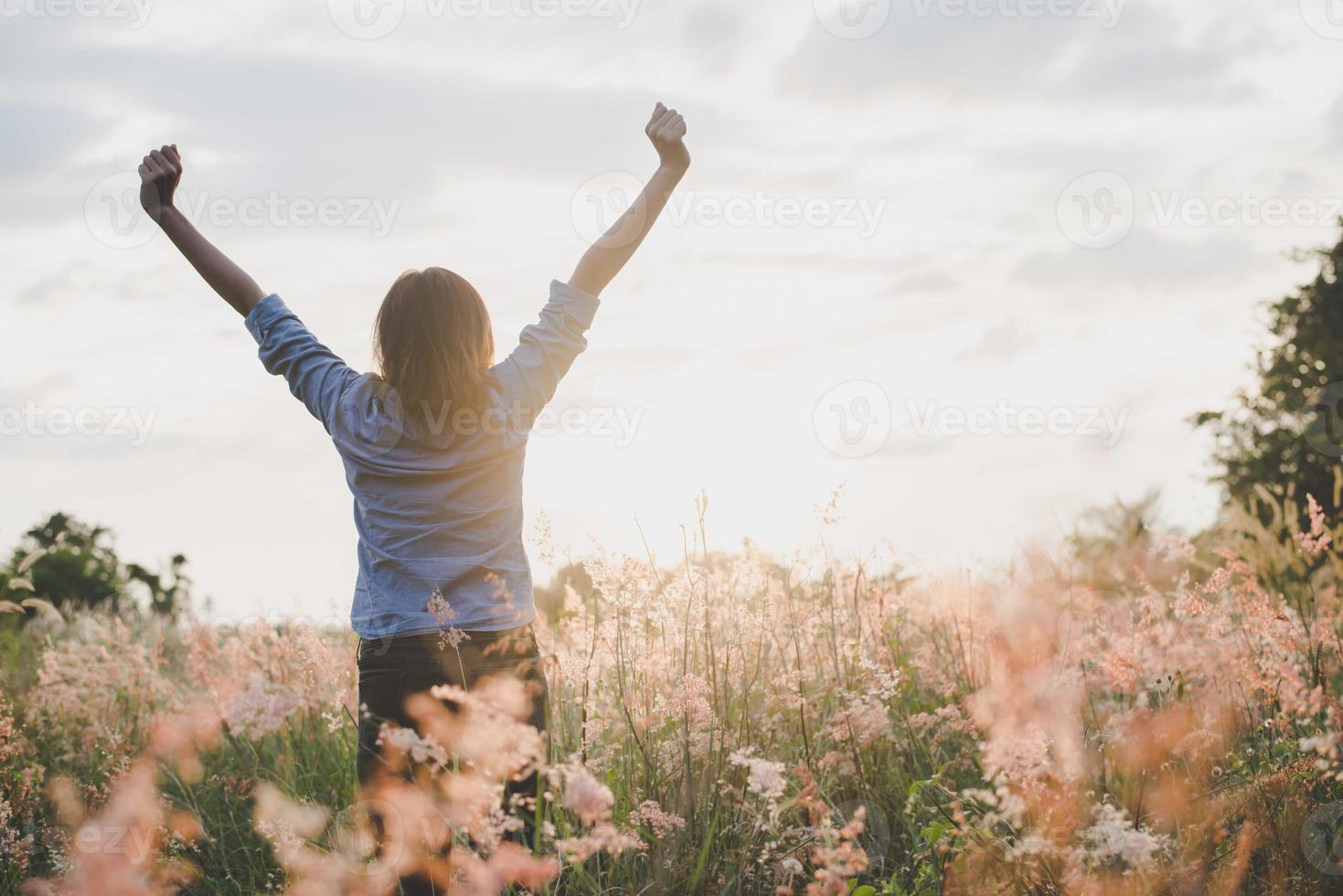 Young beautiful woman stretches her arms in the air in a field photo