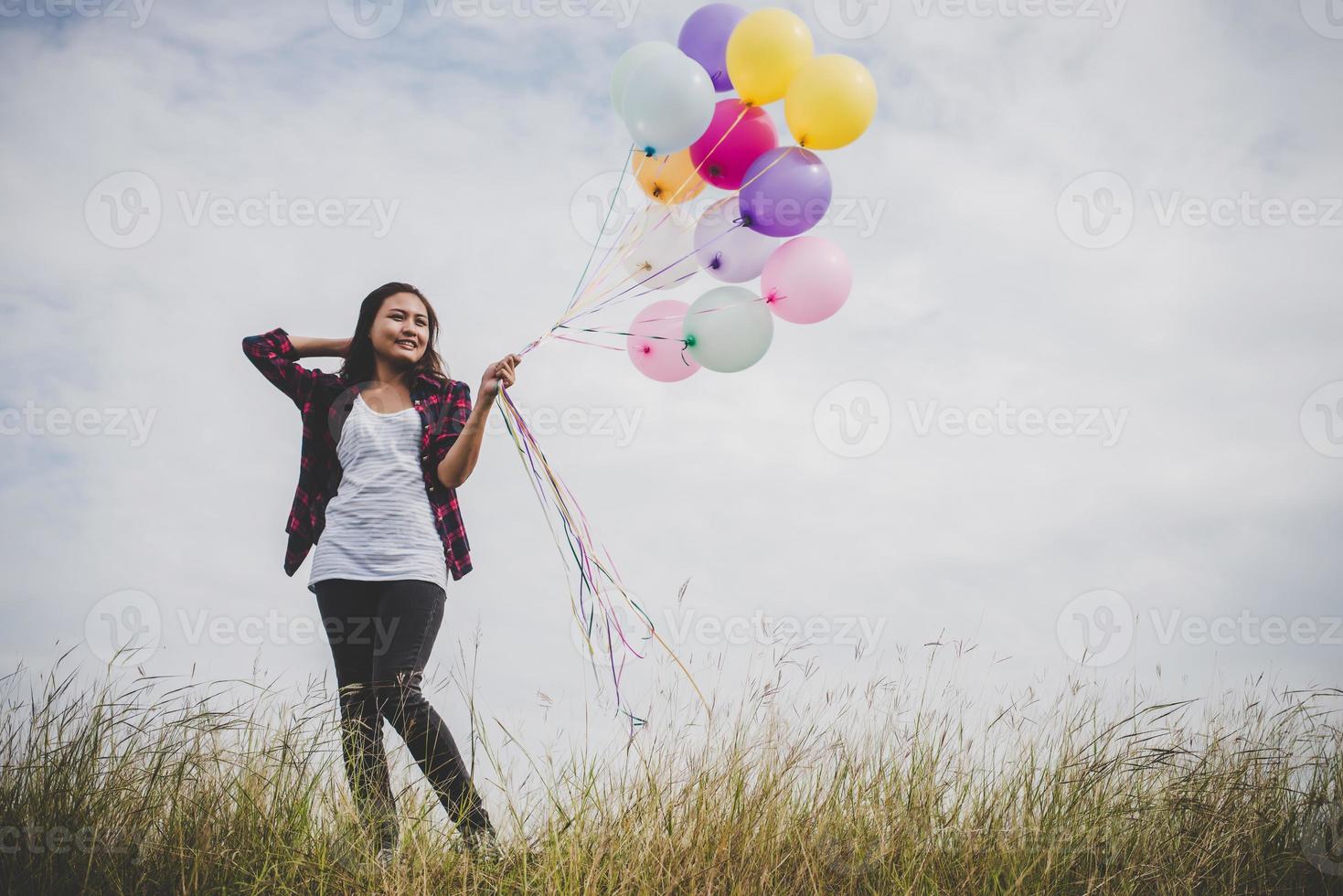 Beautiful young hipster woman holding colorful balloons outdoors photo