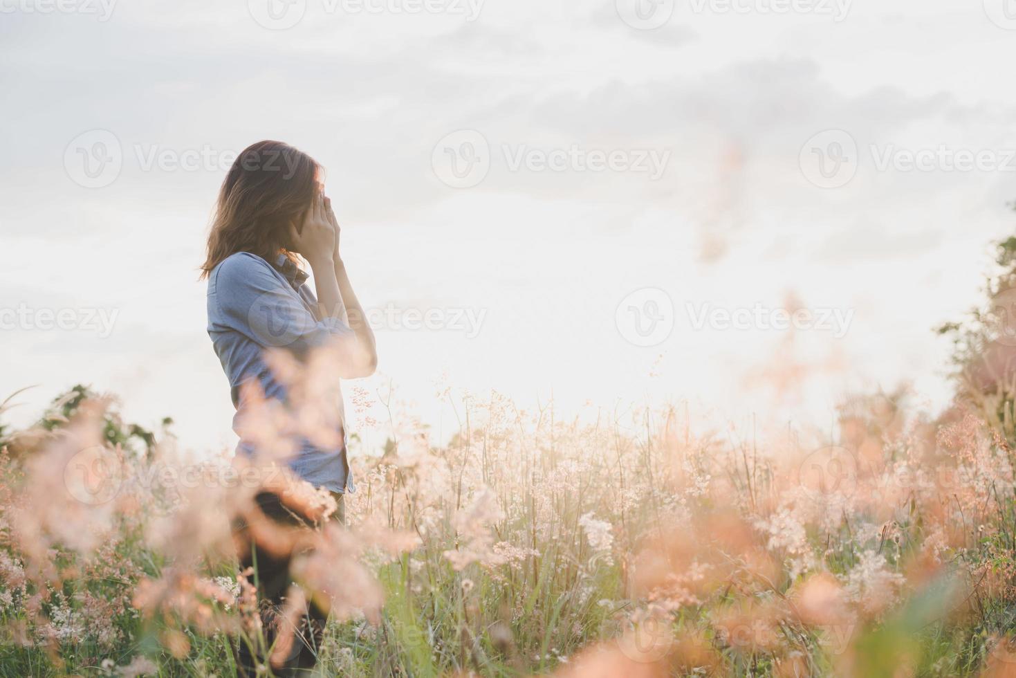 Mujer triste de pie en un campo con fondo de puesta de sol foto