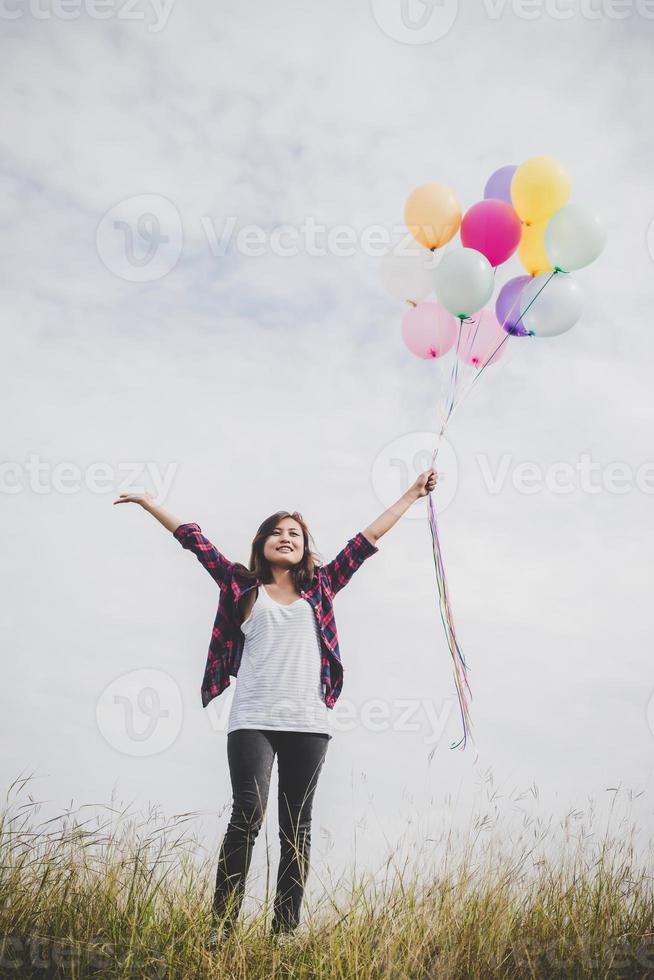 Beautiful young hipster woman holding colorful balloons outdoors photo