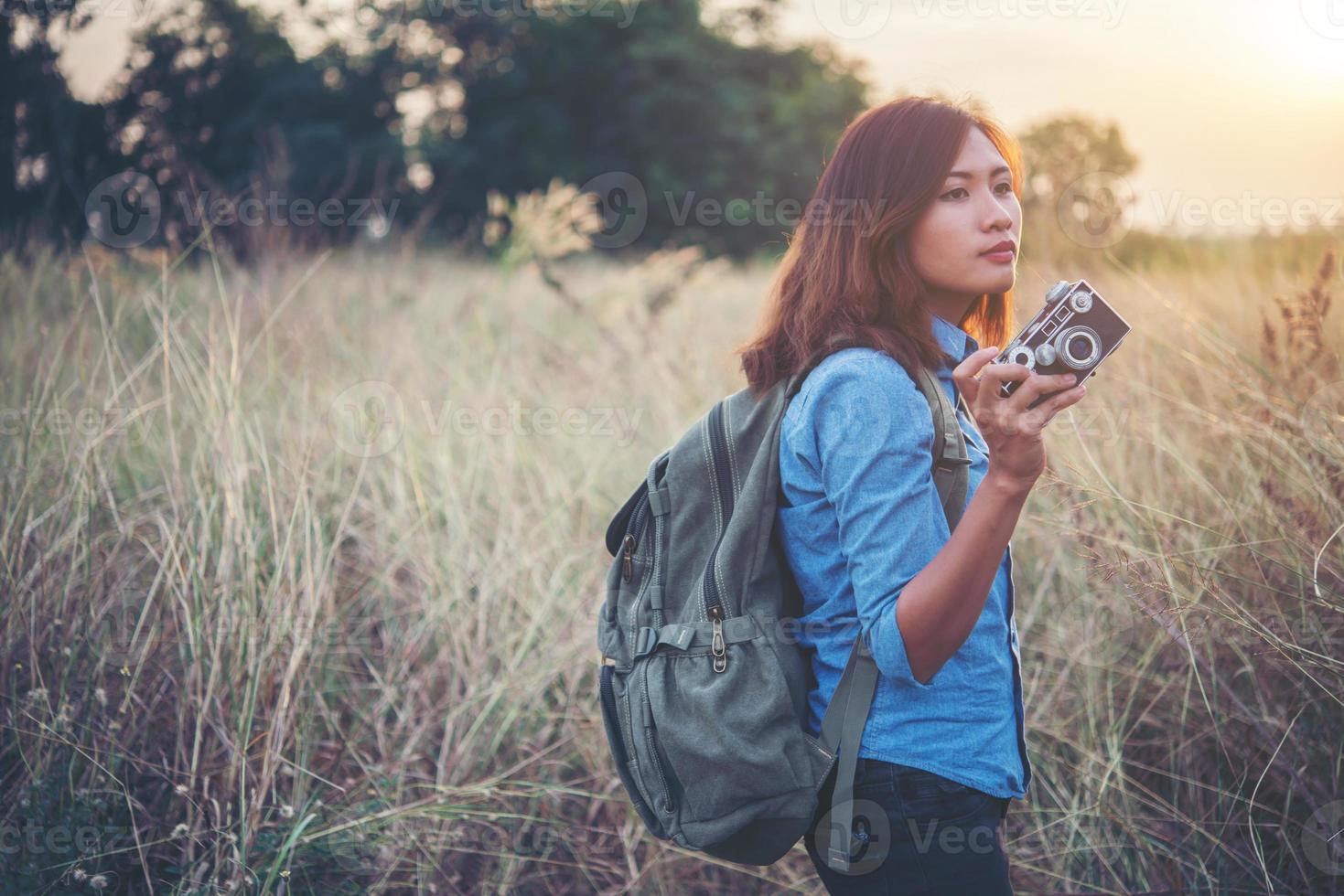 Young hipster woman backpacker with a vintage camera standing in a field photo