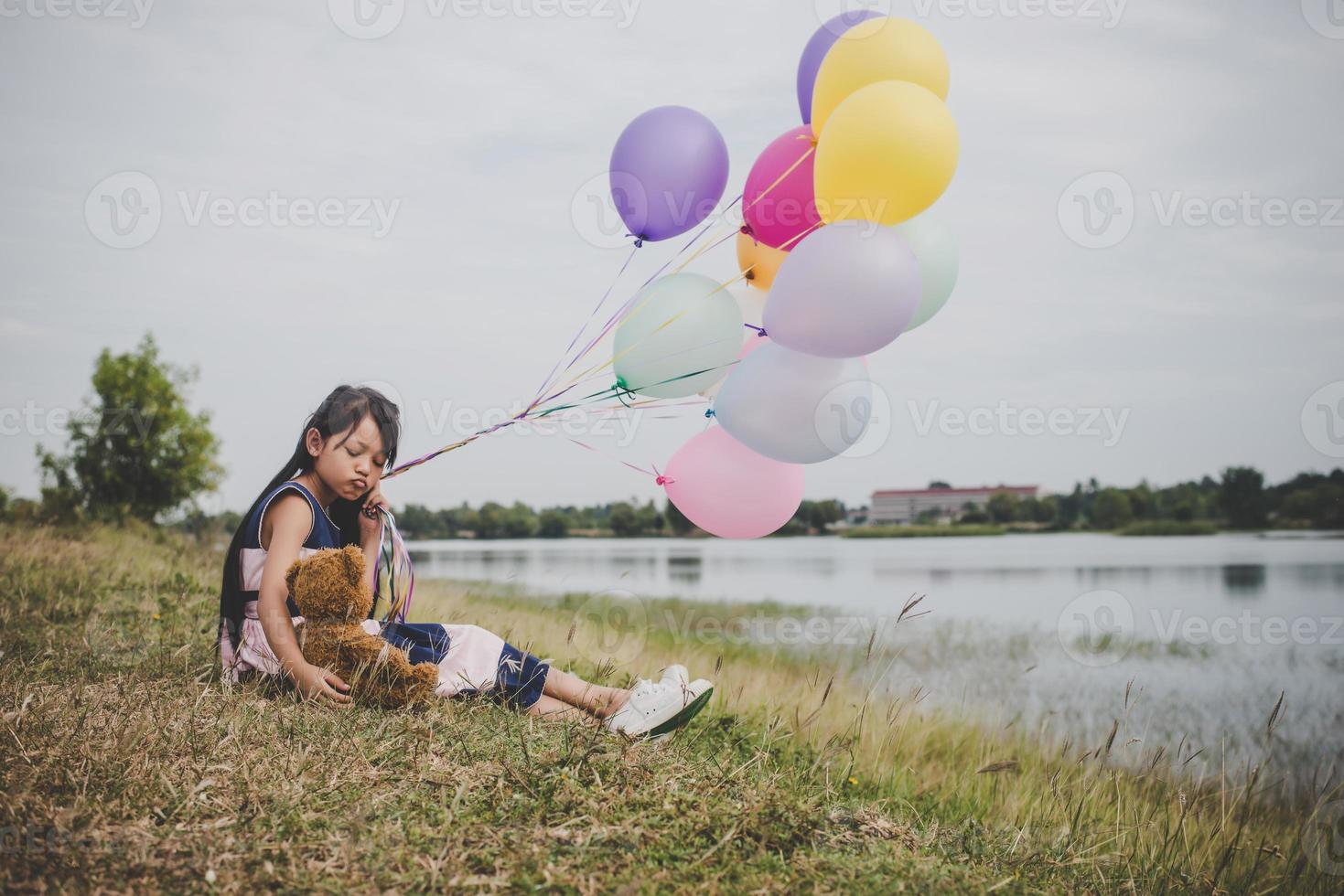 Niña con un oso de peluche y globos en el campo de la pradera foto