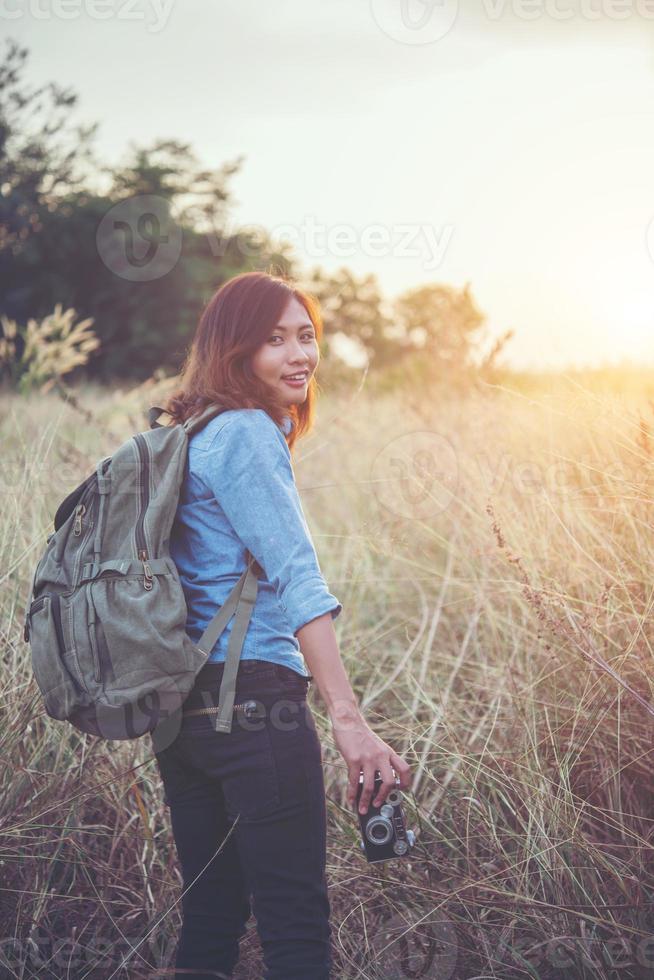 Young hipster woman backpacker with a vintage camera standing in a field photo