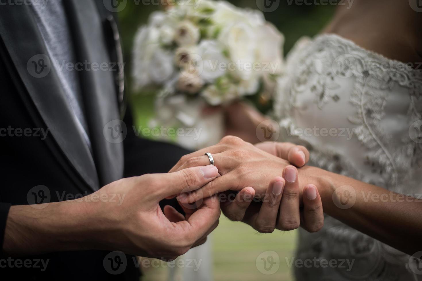 Close-up of groom putting ring on bride photo