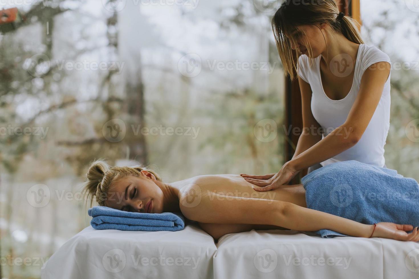 Beautiful young woman lying and having back massage in spa salon during winter season photo