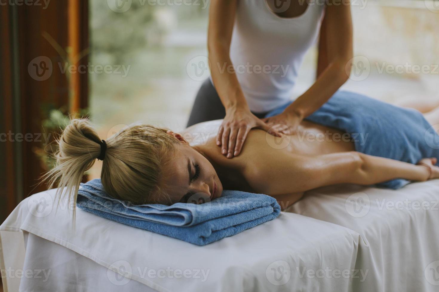 Beautiful young woman lying and having back massage in spa salon during winter season photo