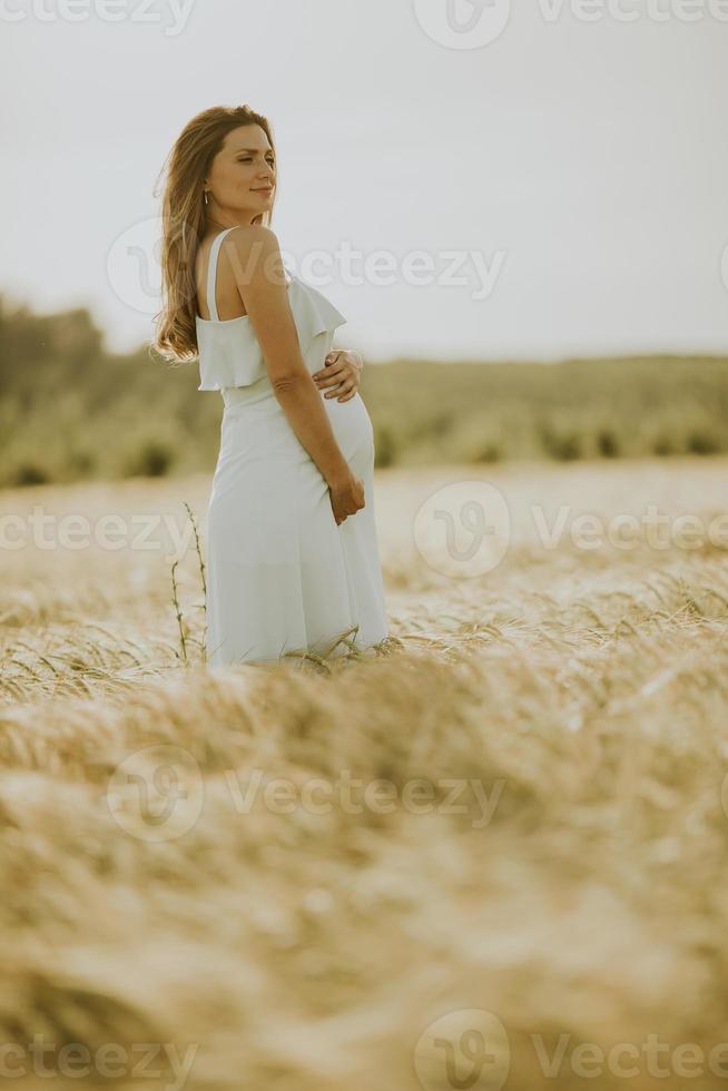 Young pregnant woman in white dress relaxing outside in nature photo