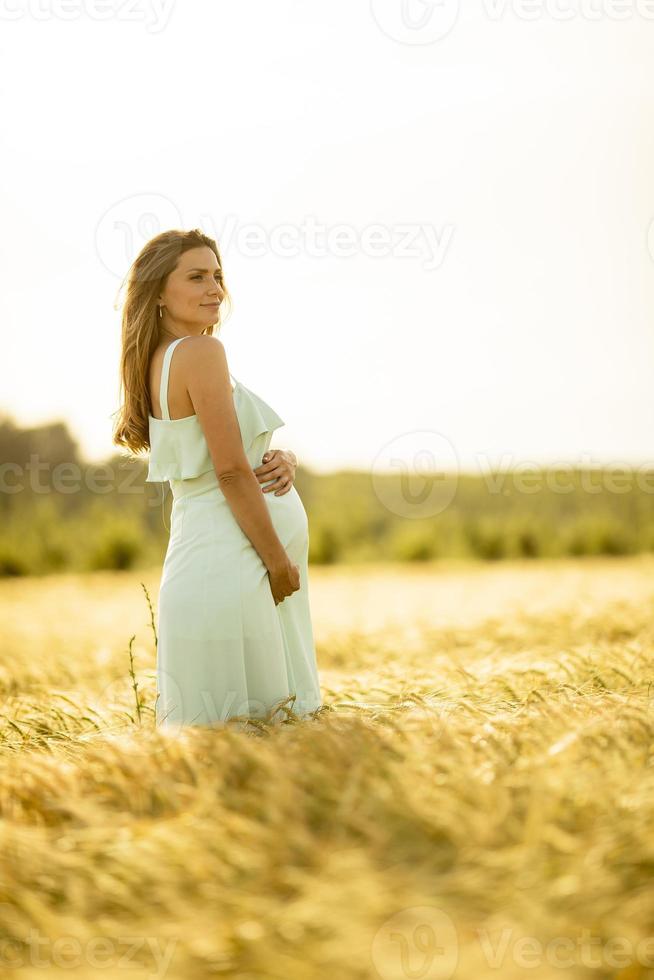 Young pregnant woman in white dress relaxing outside in nature photo