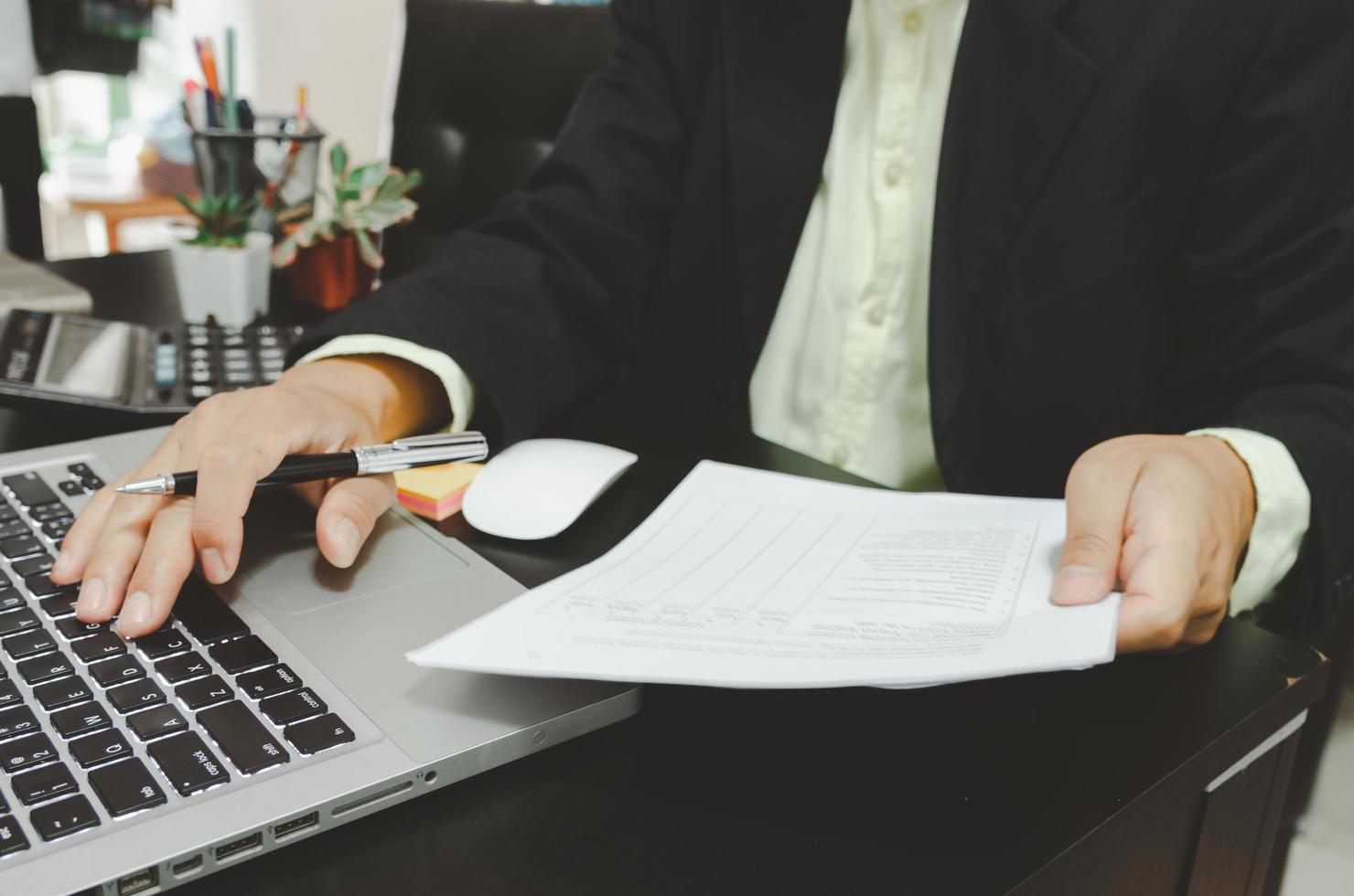 A businessman looking at business documents and holding a pen with a computer laptop and calculator at the desk working from home photo