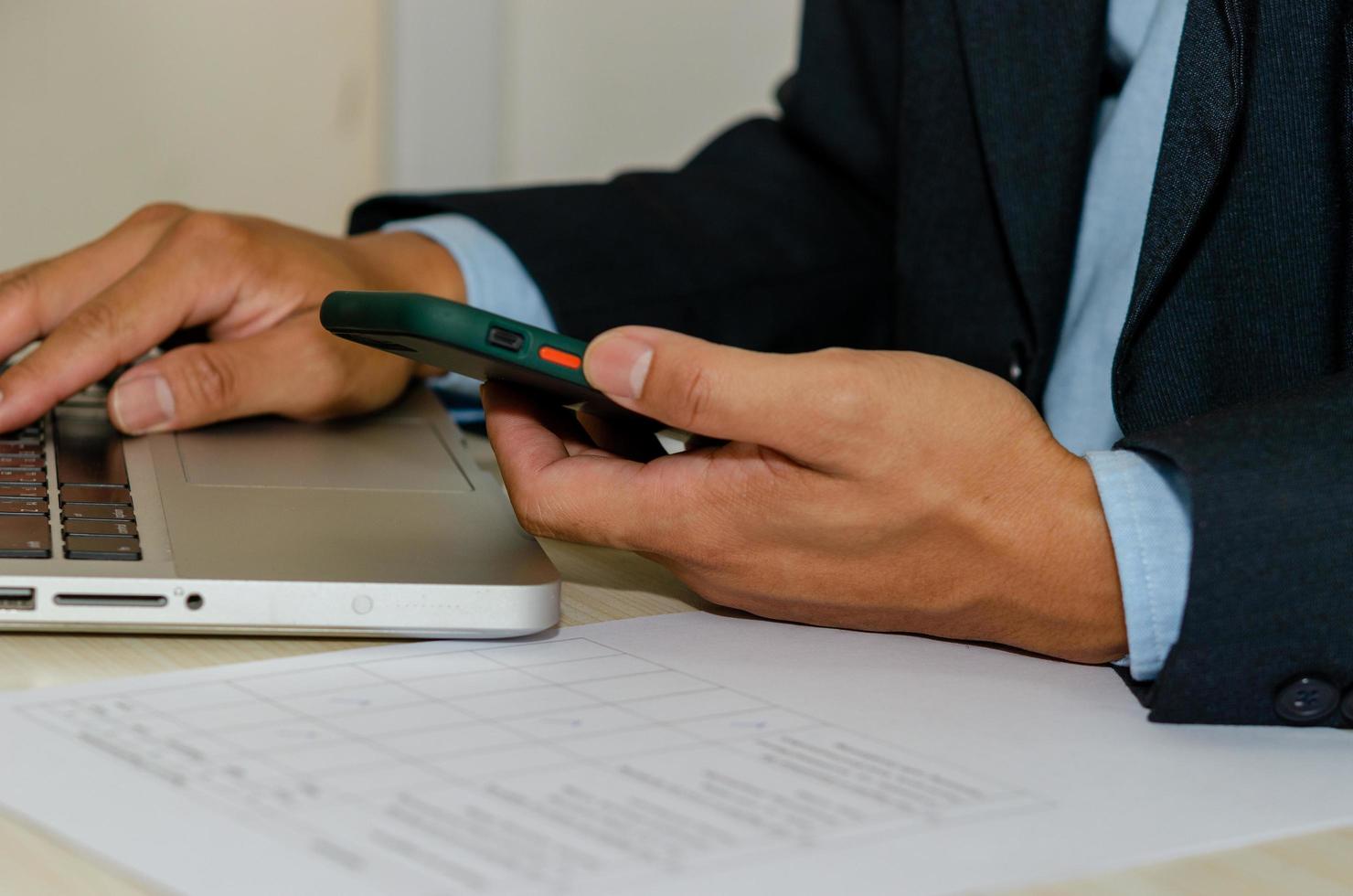 A businessman using a mobile smartphone and a computer laptop on a table searching the internet photo