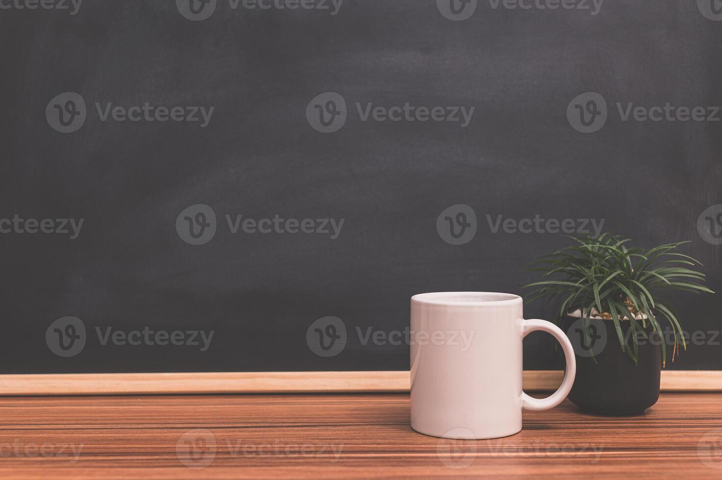 A coffee mug and plant on a wooden table in front of a blackboard photo