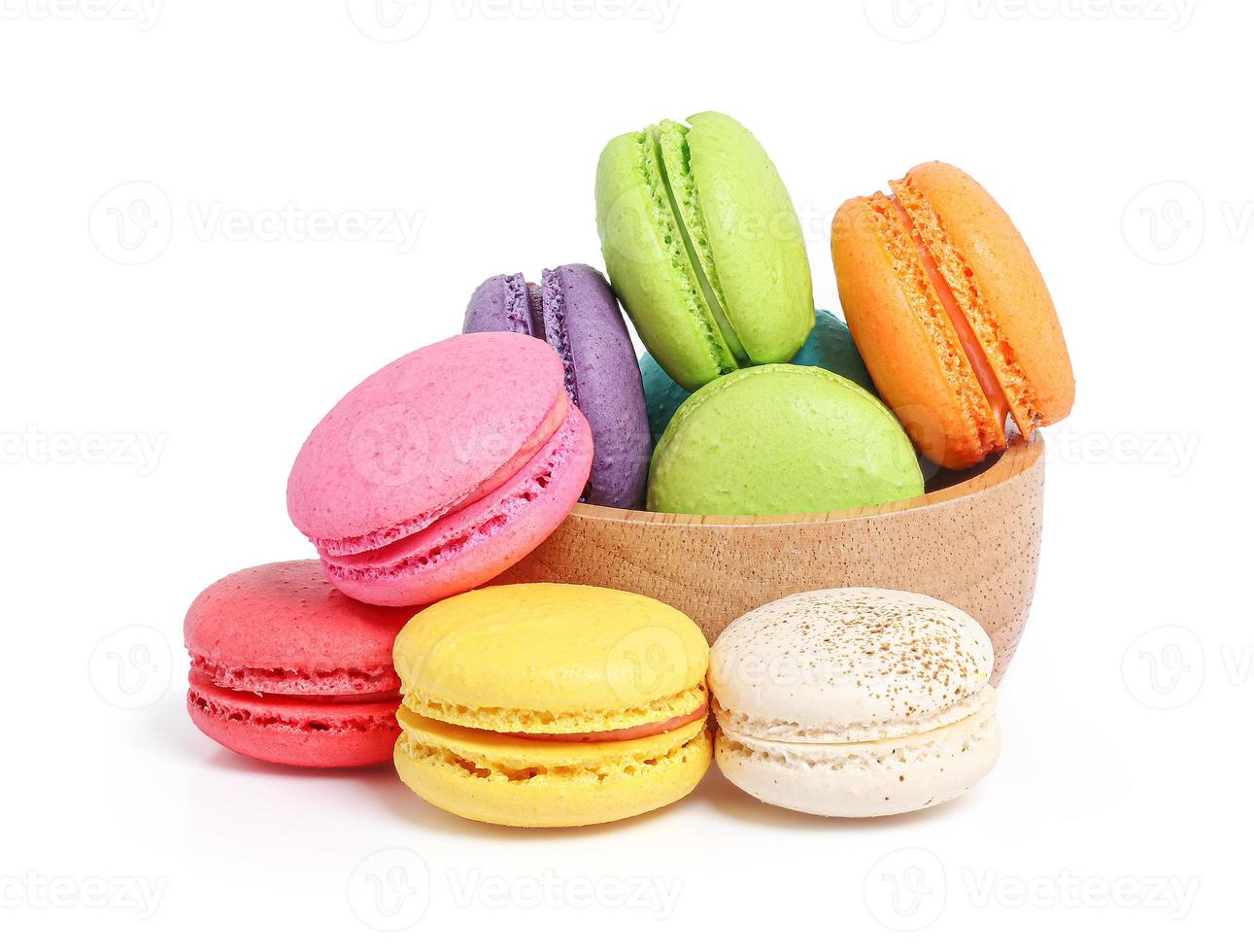 Macarons de colores en un tazón de madera sobre fondo blanco. foto