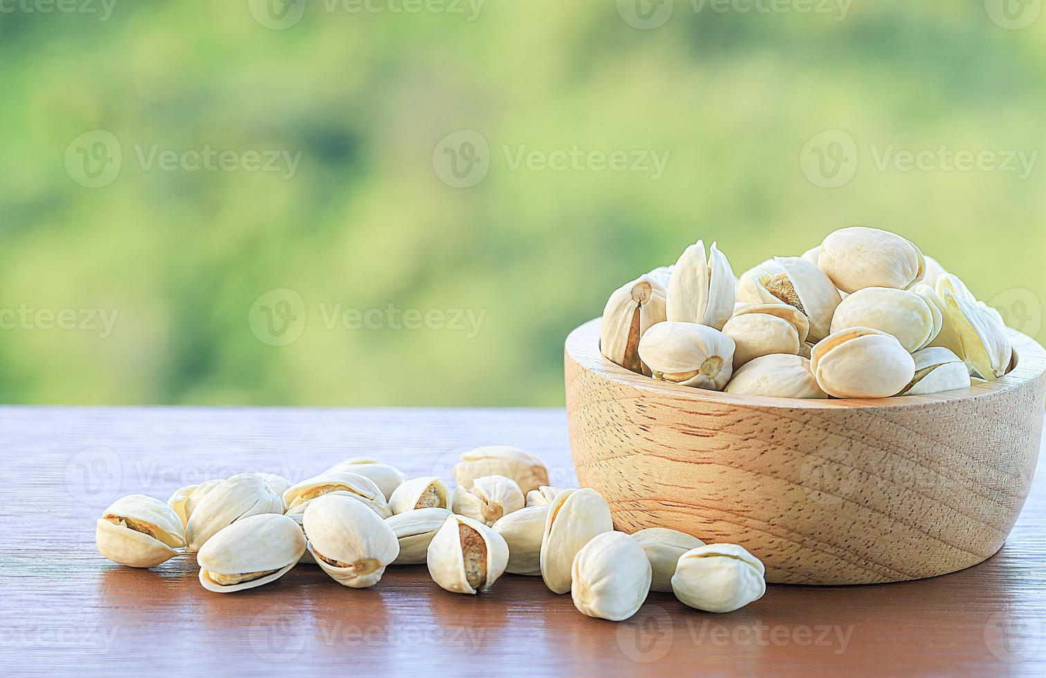 pistachos en un cuenco de madera y sobre una mesa de madera con fondo de naturaleza borrosa foto