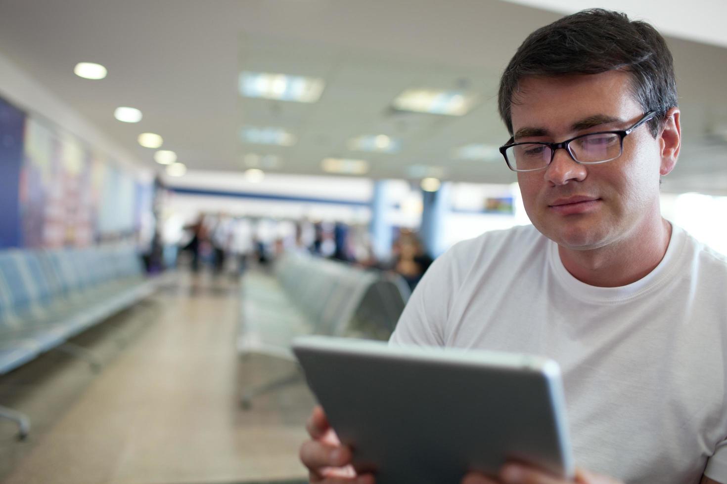 Hombre leyendo en una tableta mientras espera en el aeropuerto. foto