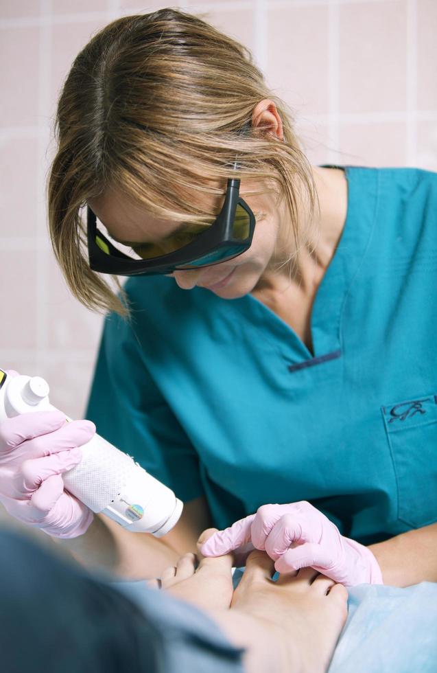 médico haciendo un tratamiento con láser en los pies de la mujer foto