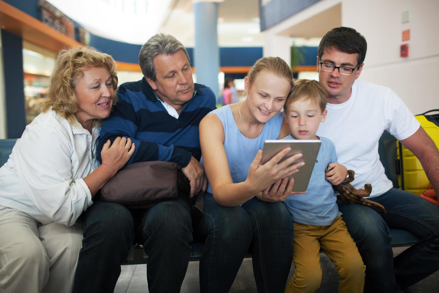 Big family looking at a tablet in an airport photo